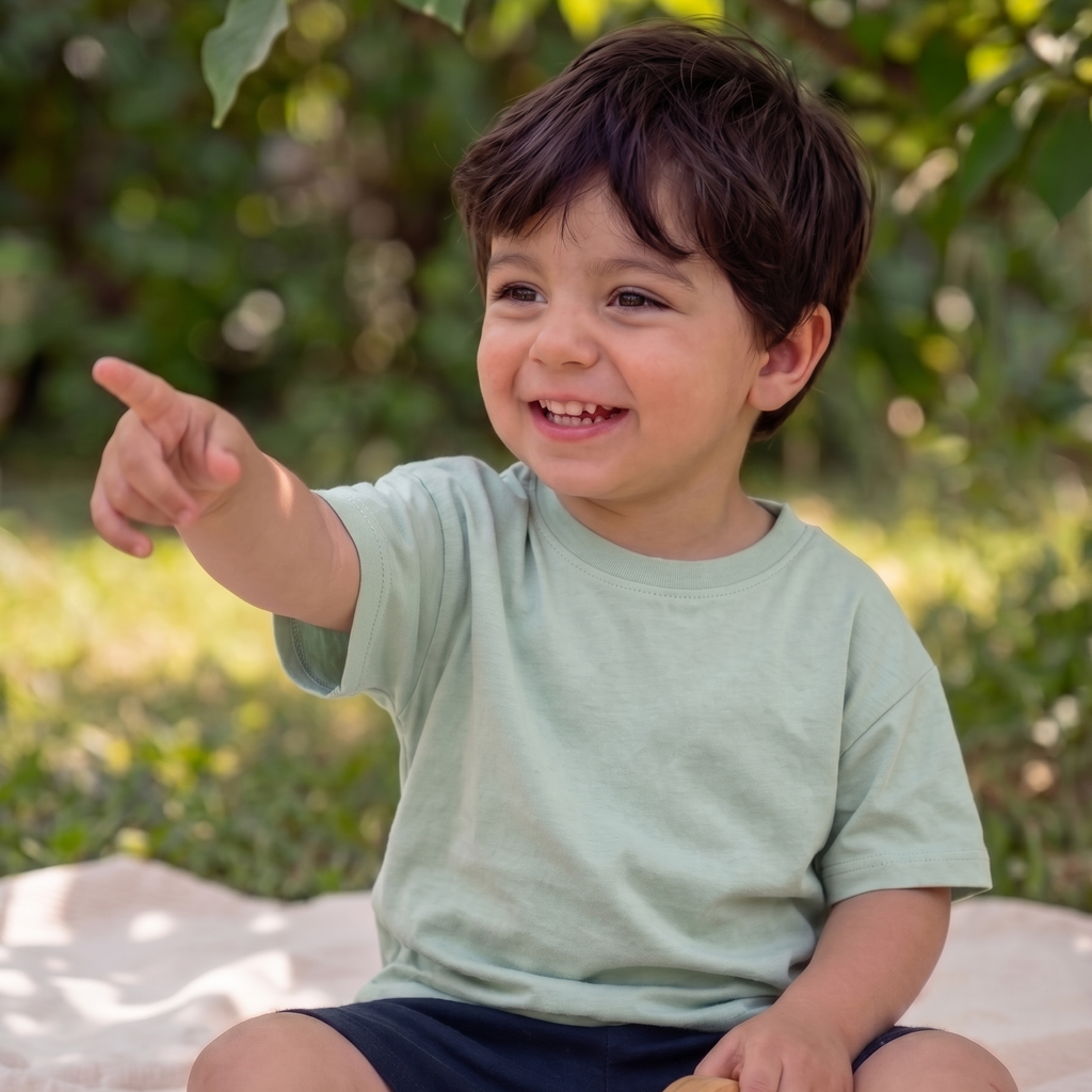 Child sitting outdoors on a blanket, holding a wooden toy, with greenery in the background