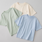 Three plain t-shirts in green, beige, and blue on a light gray background